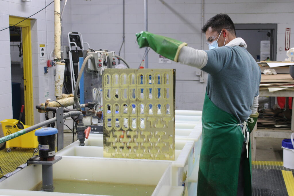 Worker in protective gear lowering a sheet of metal into plating tank.