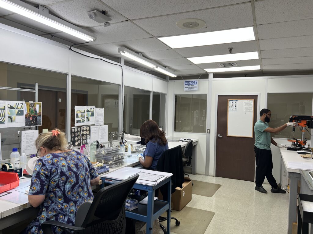 Workers seated at desks assembling and inspecting components in a production facility.
