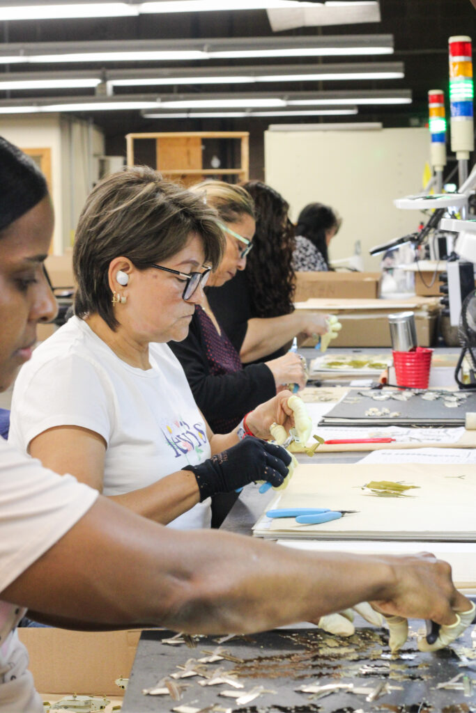 Employees seated at workstations carefully hand-finishing and assembling small components.