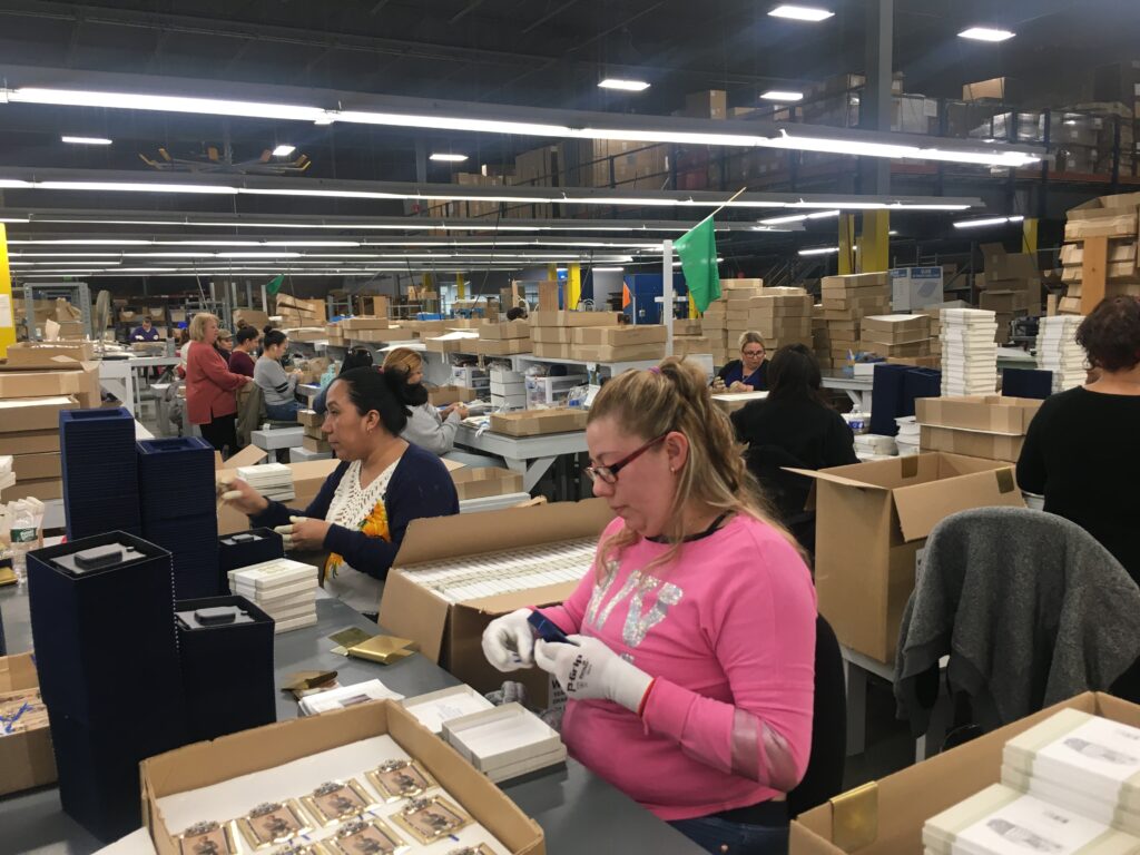 Employees in a large facility assembling and packaging products at workstations.